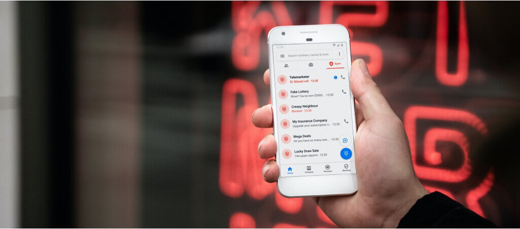 A person holding a white smartphone displaying an email inbox, with blurred red neon lights in the background.