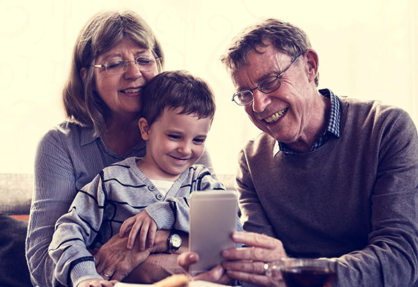 Two smiling adults and a young child are looking at a smartphone held by one of the adults. Two smiling adults and a young child are looking at a smartphone held by one of the adults.
