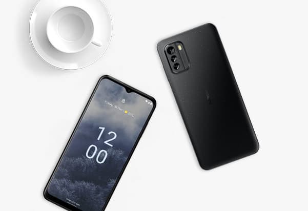 Two black smartphones on a white surface. One phone is face up. The other phone is face down. A white teacup and saucer are visible in the upper left corner. Two black smartphones on a white surface. One phone is face up. The other phone is face down. A white teacup and saucer are visible in the upper left corner.