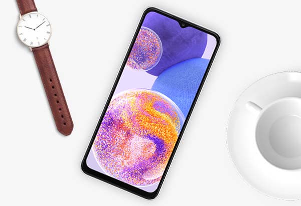 A white smartphone is positioned diagonally on a light-colored surface. To the left of the phone, a watch with a white face and a brown leather strap is visible. To the right, part of a white teacup and saucer can be seen. A white smartphone is positioned diagonally on a light-colored surface. To the left of the phone, a watch with a white face and a brown leather strap is visible. To the right, part of a white teacup and saucer can be seen.
