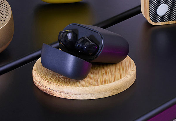 OneSonic MXS-HD1 noise cancelling wireless earbuds resting in their open charging case, placed on a wooden charging pad on a dark desk surface.
