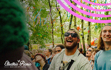 Electric Picnic festival-goers enjoying the event in a woodland setting with Three+ branding.