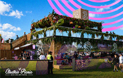 Three-branded Electric Picnic festival stage decorated with greenery and surrounded by festival-goers.