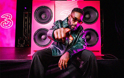 Tinie Tempah performing on stage in front of large speakers with Three branding.