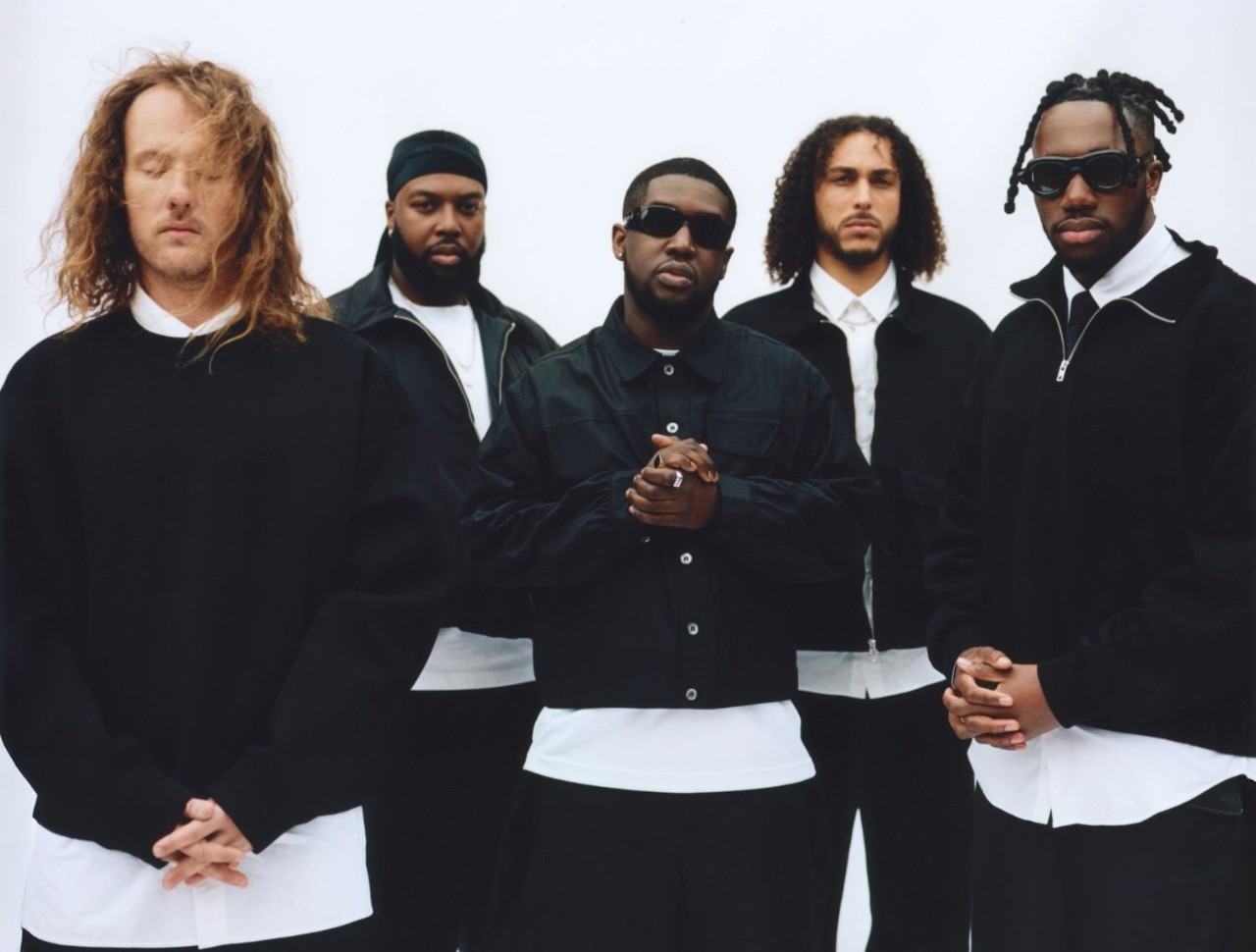 Ezra Collective posing together in black and white clothing against a plain background.
