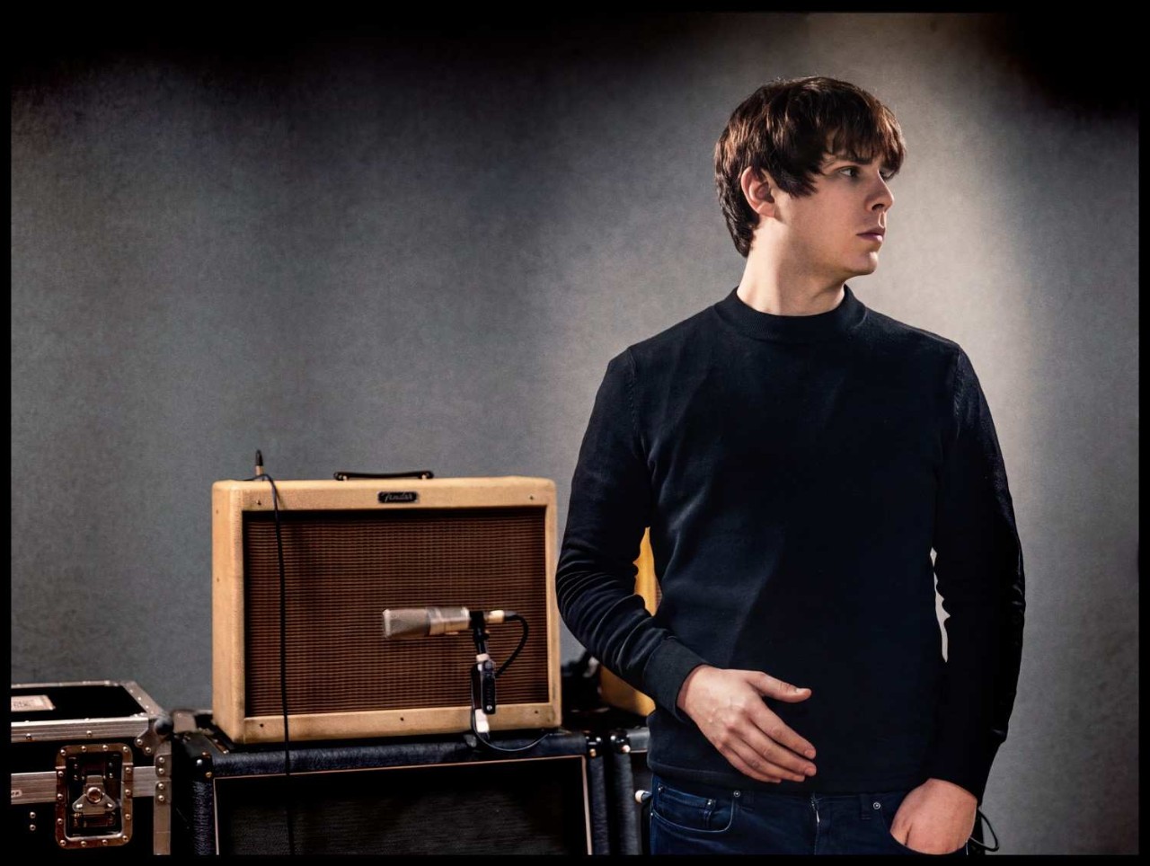 Jake Bugg posing beside a guitar amplifier and microphone to promote his new tour.
