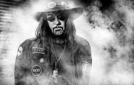 Ministry band photo - black and white portrait of frontman in wide-brim hat, sunglasses, and chin tattoo, standing in dramatic smoke