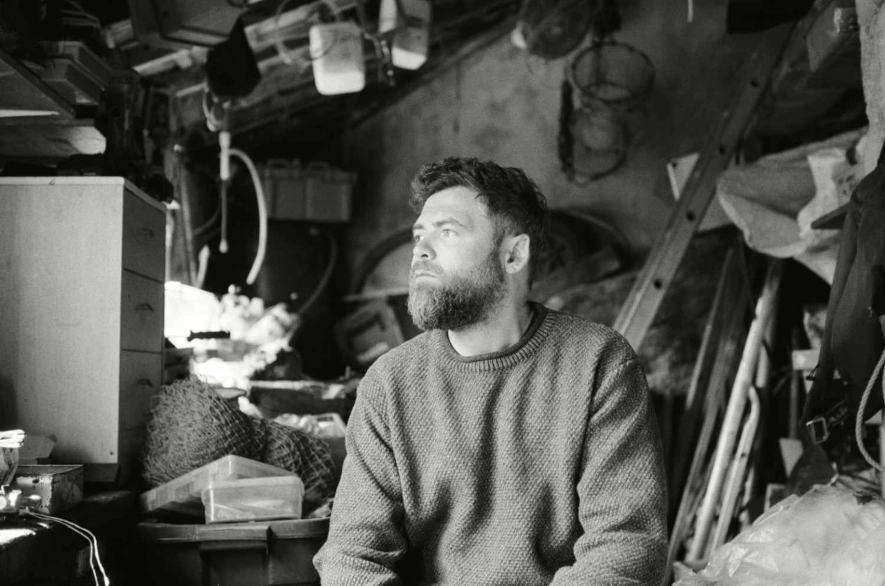 Passenger promotional image for his new tour, showing him seated in a workshop wearing a knitted jumper