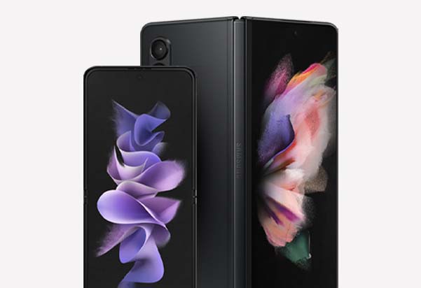 The Samsung Galaxy Z Flip3 and Z Fold3 in Phantom Black shown together, with the Flip3 folded vertically in the foreground and the Fold3 partially unfolded behind it, both displaying vibrant floral wallpapers.
