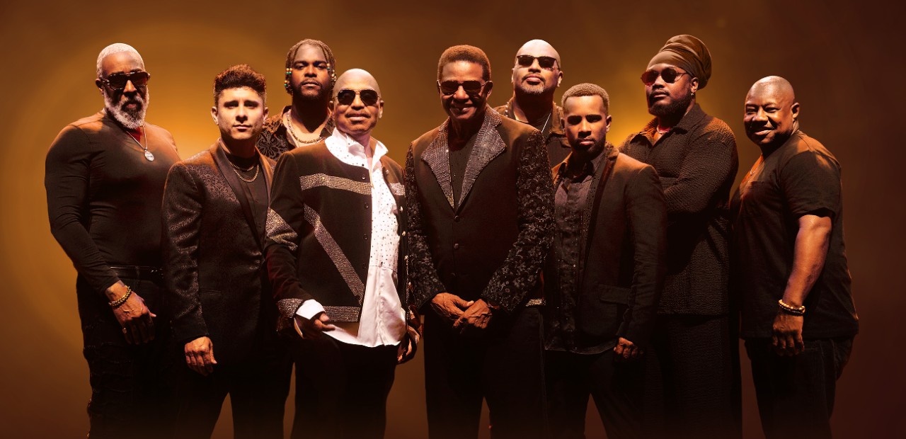 Promotional image of The Jacksons standing together in black outfits against a gold background for their latest tour