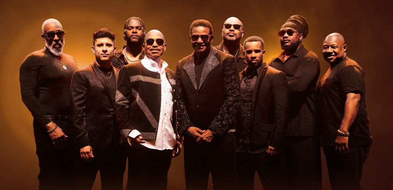 Promotional image of The Jacksons standing together in black outfits against a gold background for their latest tour