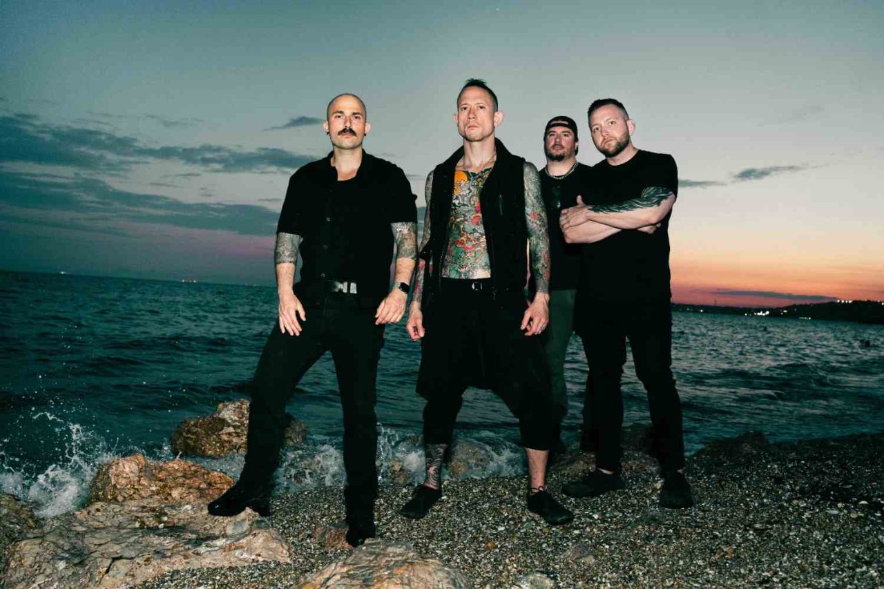 Trivium posing on a rocky shoreline at sunset.