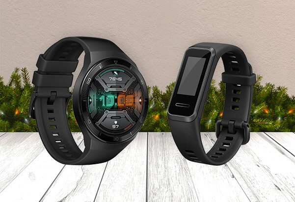 A Huawei Watch GT2e smartwatch and Huawei Band 4 fitness tracker, both in black, displayed side by side in a festive Christmas setting with pine garland in the background.