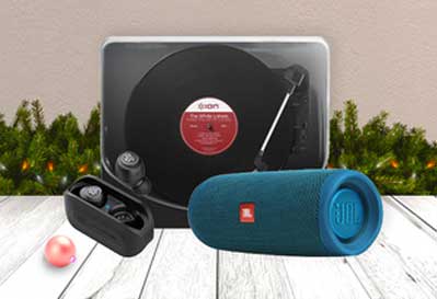An ION portable turntable, JBL Flip Bluetooth speaker in teal, and black wireless earbuds displayed together in a festive Christmas setting.