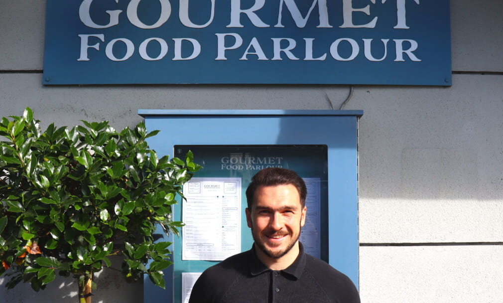 A man standing in front of the Gourmet Food Parlour restaurant sign