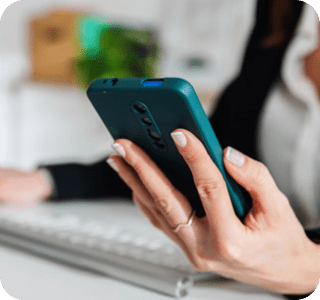 Person sitting at a desk in front of a computer looking at a phone Person sitting at a desk in front of a computer looking at a phone