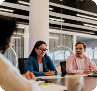 Three individuals seated at a conference table engaged in discussion during a meeting. Three individuals seated at a conference table engaged in discussion during a meeting.