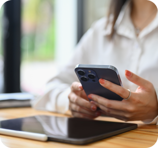 Person sitting at a desk holding at a phone, on the desk is also a tablet.