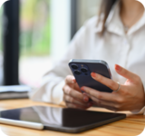 Person sitting at a desk holding at a phone, on the desk is also a tablet.