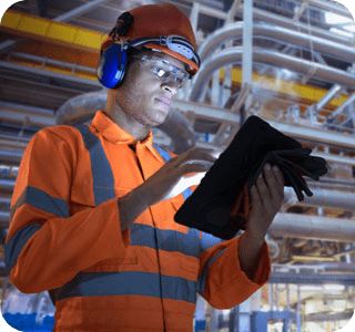 Person wearing a hi-vis vest with hard hat and ear protection in an industrial workplace, using a tablet Person wearing a hi-vis vest with hard hat and ear protection in an industrial workplace, using a tablet