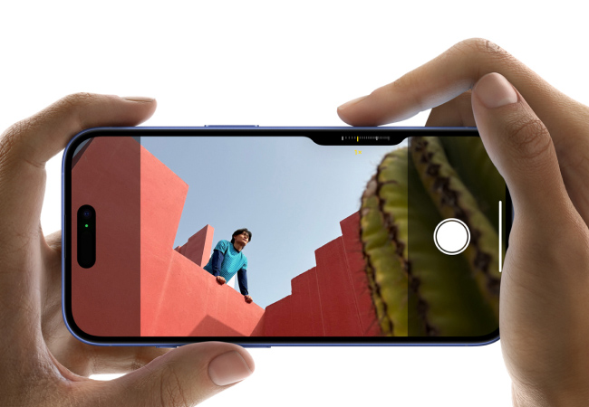  Hands hold a blue iPhone, showing a person on red steps and a cactus on its screen, in landscape orientation.