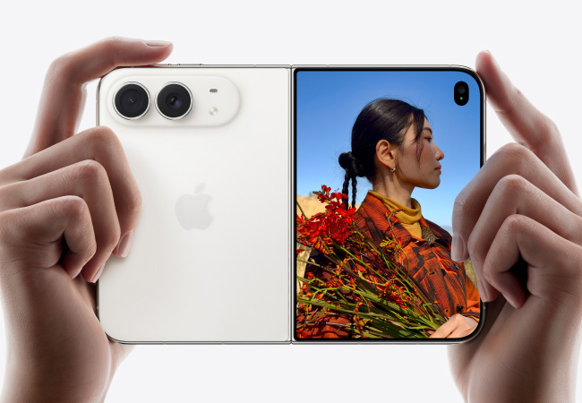 Hands holding an open silver-white iPhone Duo, showing its rear dual-camera shell on the left side and a cover/inner screen preview of a woman with red flowers on the right.