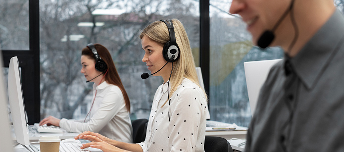 A row of three customer service agents with headsets on, working at their computers in a bright, modern office.