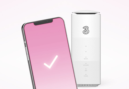 A smartphone with a pink screen and a white checkmark in the foreground, positioned in front of a white Three 5G Broadband Hub. The router shows the Three logo and its standard indicator lights, set against a clean white background to suggest successful connectivity or setup.