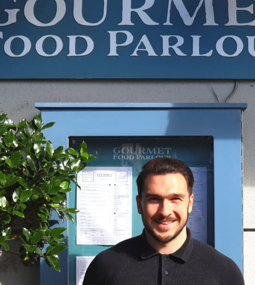 Person standing in front of Gourmet Food Parlour menu