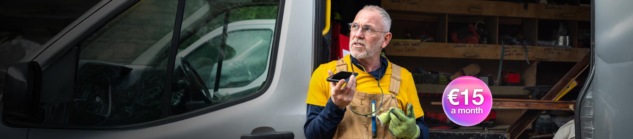 Person standing in front of an open work van, wearing overalls and a toolbelt talking on the phone.