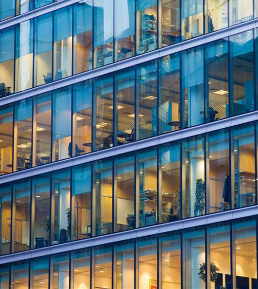 Outside view looking at several offices, people gathered in some of the offices working and holding meetings