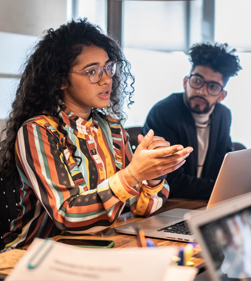 Two people sitting at a desk having a discussion while looking at a laptop