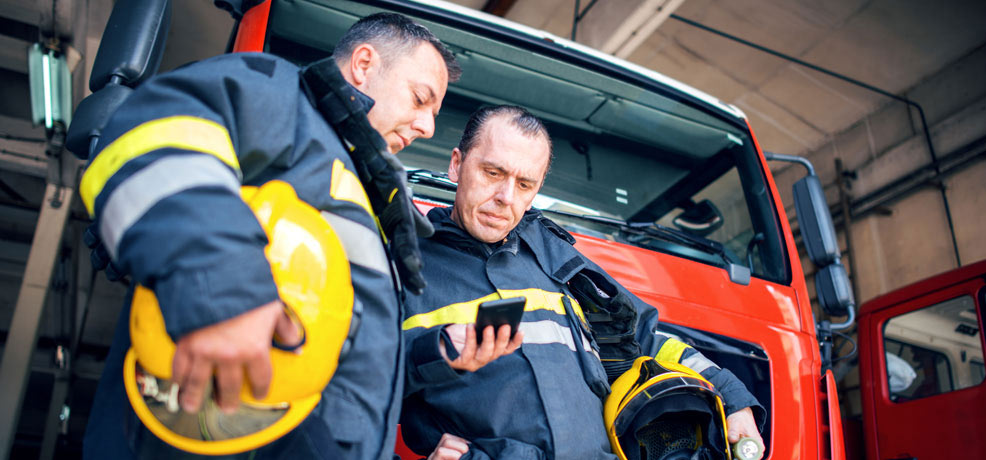 Two firefighters standing in front of a fire engine looking at a phone