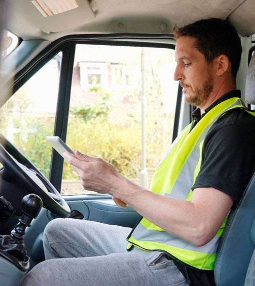 Delivery person sitting in the driver's seat in a truck, checking a tablet