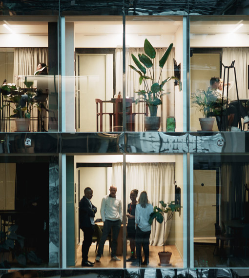 Outside view looking at several offices, peolpl gathered in some of the offices working and holding meetings