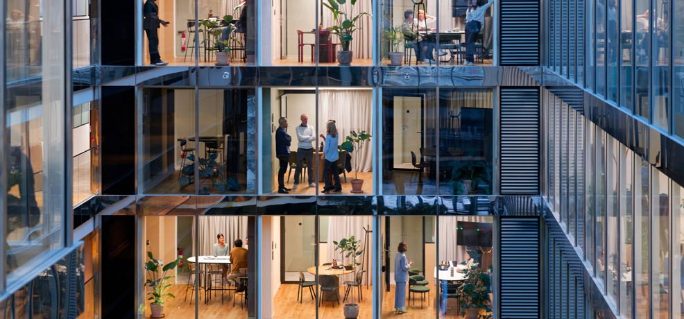 Outside view looking at several offices, peolpl gathered in some of the offices working and holding meetings