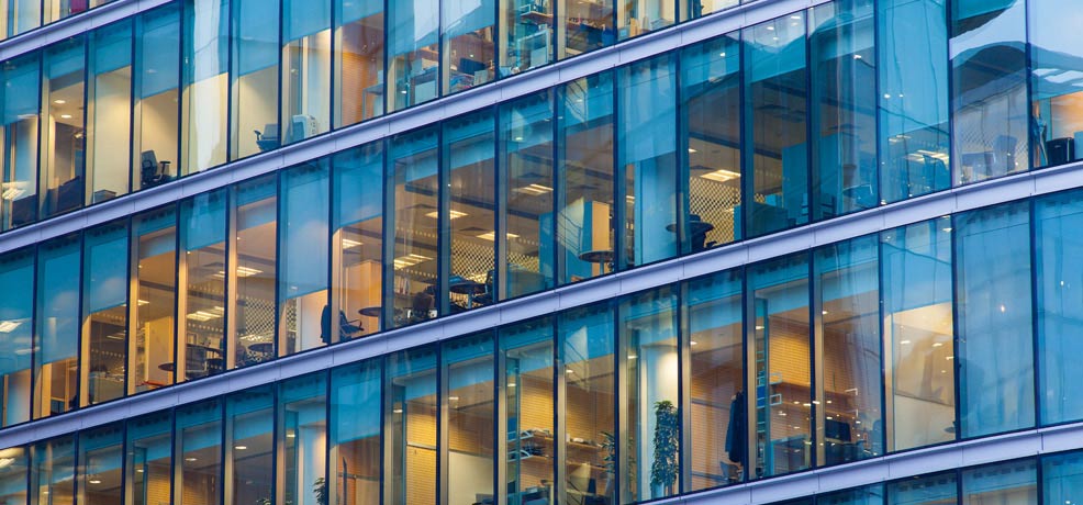Outside view looking at several offices, people gathered in some of the offices working and holding meetings