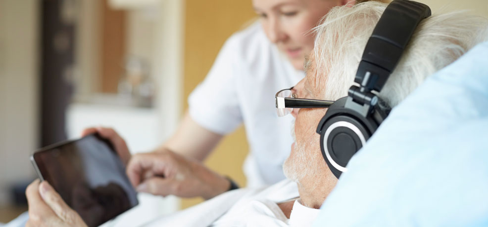 Person lying in a hospital bed, wearing headphones, appears relaxed and engaged with audio content.