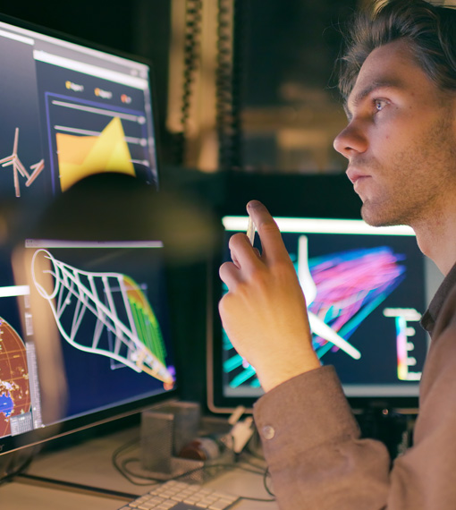 Person working at a desk in a darkened room in front of multiple monitors showing different graphs