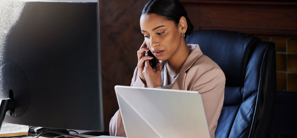Person seated at a desk, working on a laptop while talking on a phone