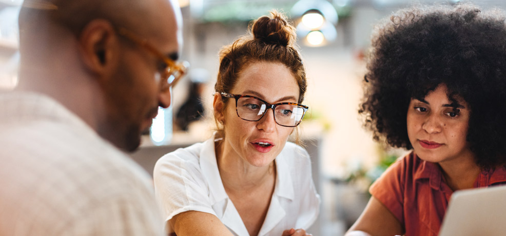 Three people sitting around a laptop, having a discussion.
