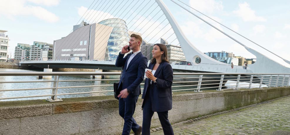 Two business people walking along the quays of the Liffey in Dublin city, near a bridge, discussing work matters.