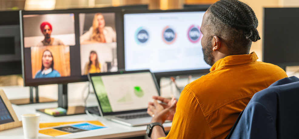 Person at a desk with a laptop and two screens having a video conference.