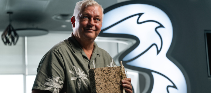 CEO of Tao Climate holds a block of a fibrous, brick-like material. He stands in front of a wall with a lit-up "3" logo.
