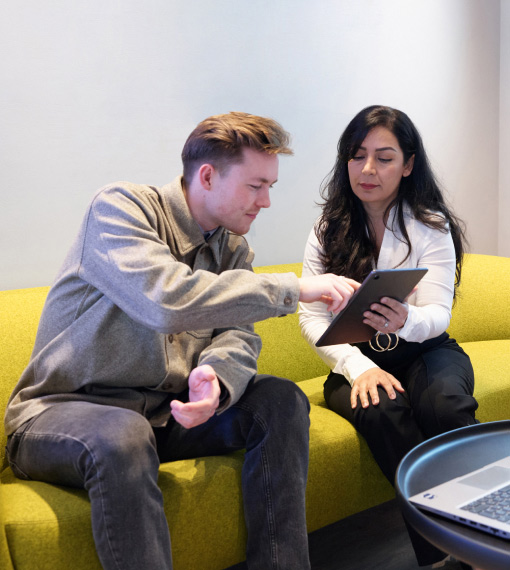 Two people sitting together on a couch having a discussion while looking at a tablet