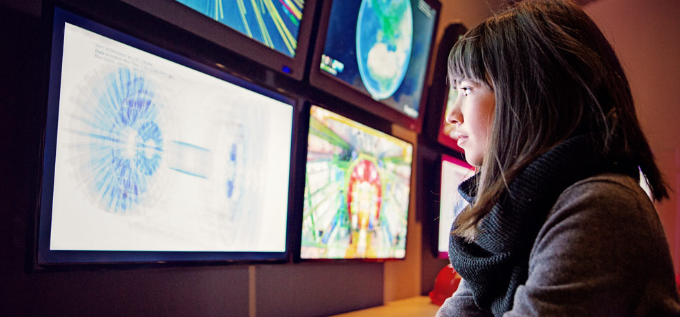 A woman gazes at a display featuring multiple television screens showcasing various images.