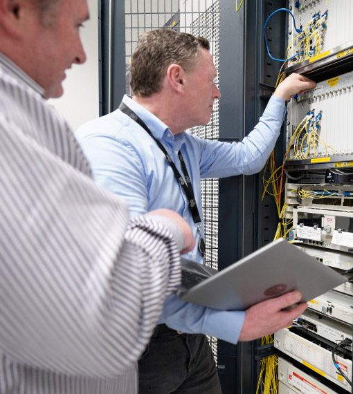 Two people are in a room full of servers, examining a computer together, engaged in conversation.