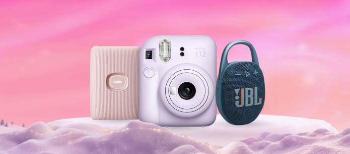 A pastel pink photo printer, a lavender Instax instant camera, and a dark blue JBL Clip portable speaker with a carabiner clip, displayed on a pink, snowy platform.