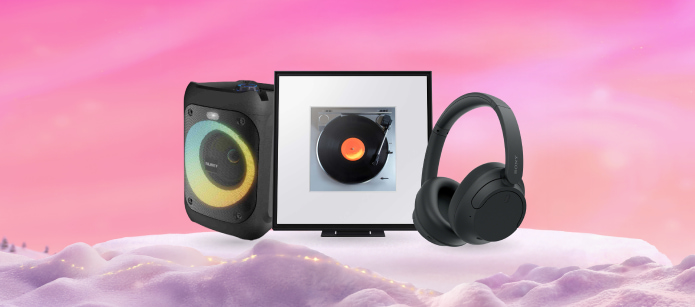A black portable Majority speaker with a rainbow LED ring, a Samsung Music Frame with a picture of a turntable playing a vinyl record, and a pair of black over-ear headphones, all on a snowy pink platform.