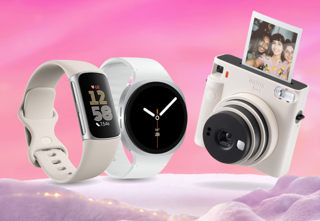 Three gadgets on a pink, snowy background: a beige fitness tracker, a white smartwatch, and a white instant camera printing a photo of three people smiling.